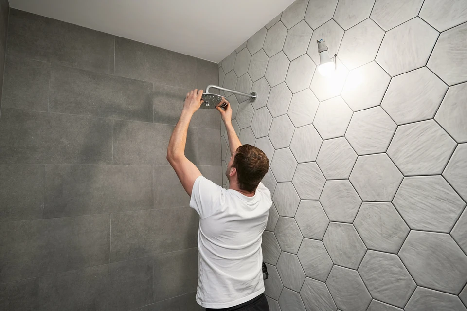 Un ouvrier masculin réparant la tête de douche de la salle de bain en travaillant à la rénovation de la salle de bain