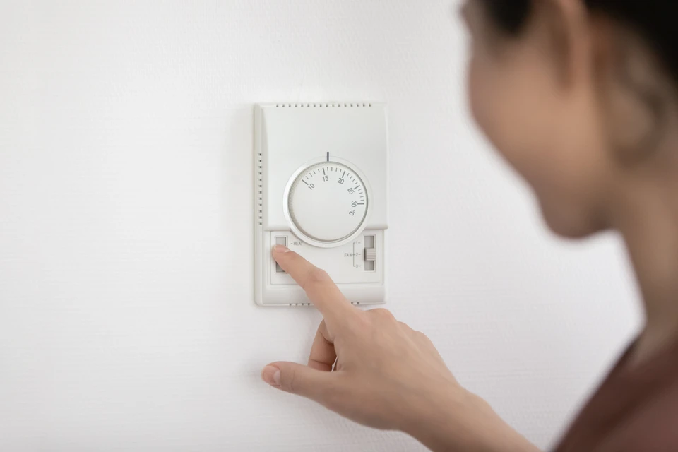 Une personne ajuste un thermostat mural blanc dans un intérieur résidentiel