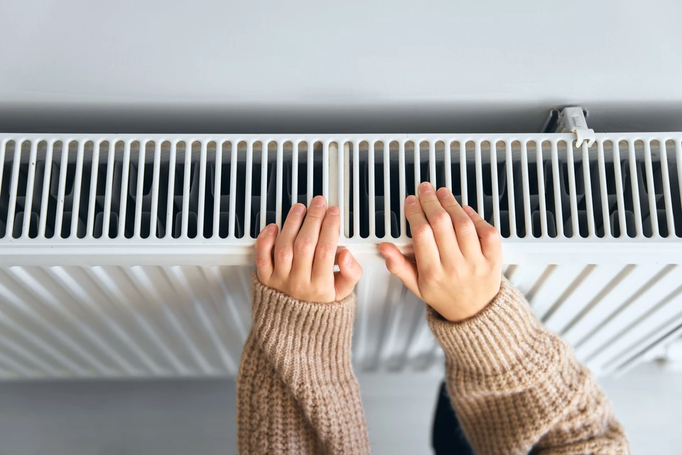 Une main portant un gant de protection bleu manipule une clé de purge sur un radiateur blanc à panneaux