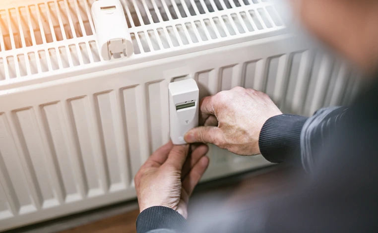 Homme en t-shirt gris ajustant un robinet thermostatique de radiateur dans un intérieur résidentiel