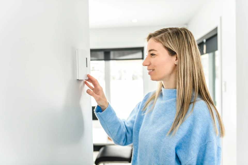 Une personne ajuste un thermostat mural blanc dans un intérieur résidentiel